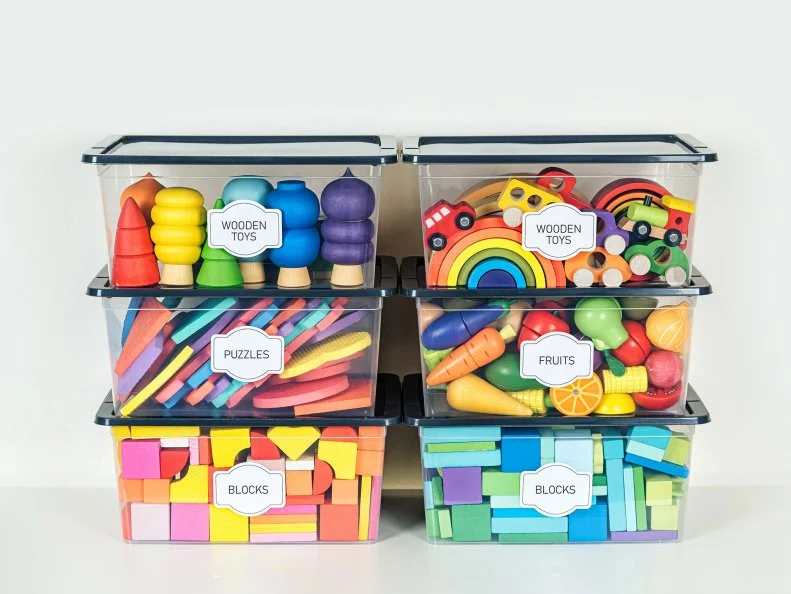 Six labeled clear bins stacked in two columns, sorting wooden toys by category, including blocks and puzzles.