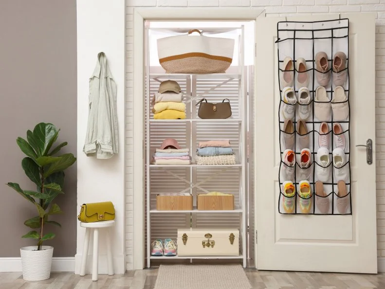 A tidy closet with a shelving unit of folded clothes and bins, plus an over-the-door shoe organizer.