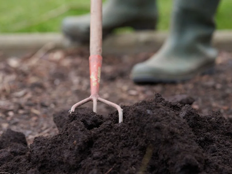 Person adding compost into soil with hand hoe.