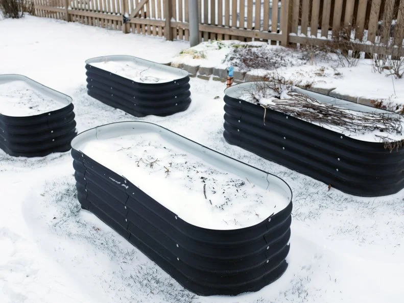 Four metal raised garden beds covered in snow.