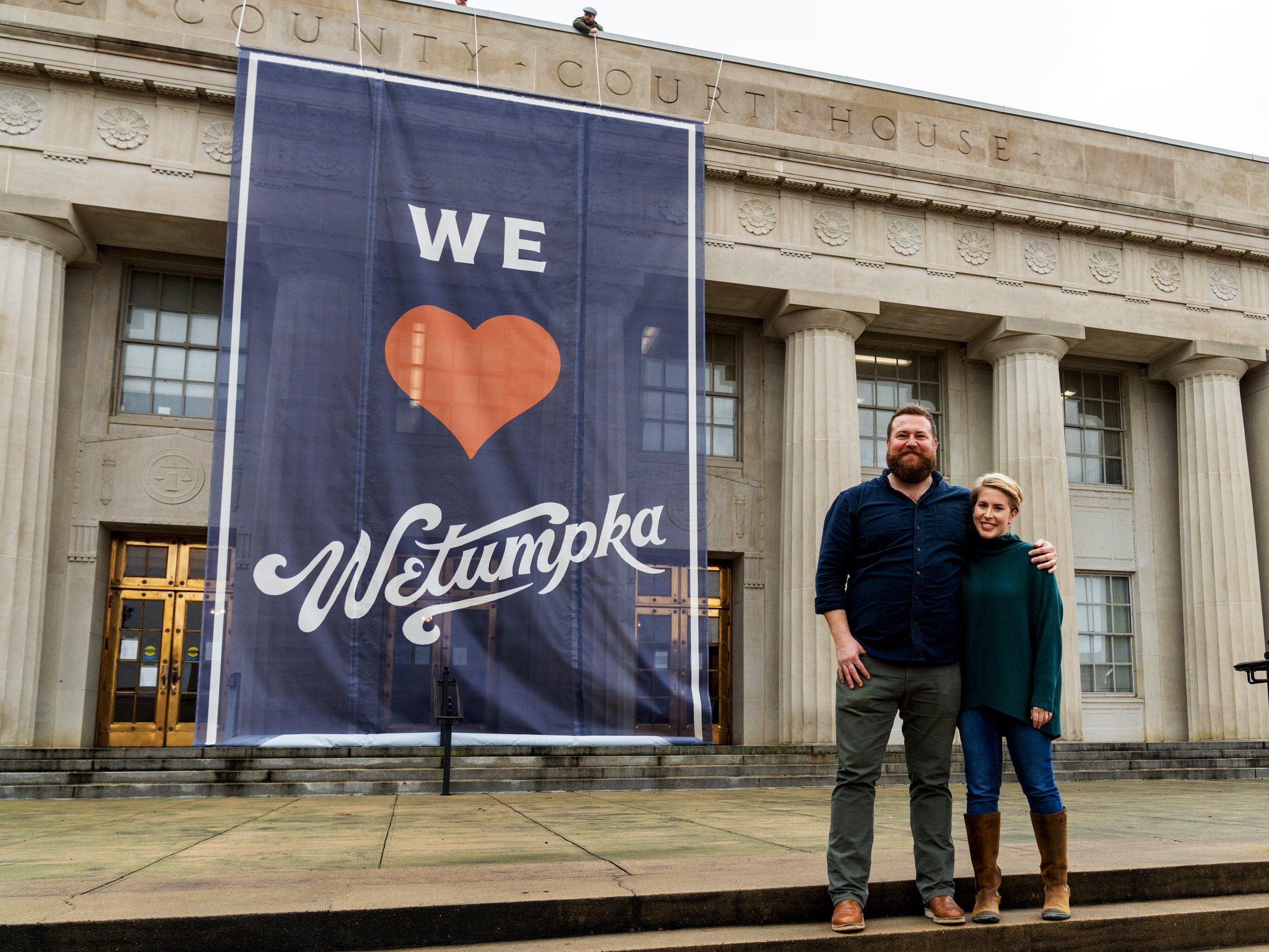 As seen on Home Town Takeover, Ben and Erin Napier pose during the reveal of a large banner at Elmore County Court House in Wetumpka, Alabama.