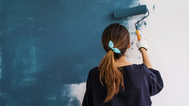 Young asian happy woman painting interior wall with paint roller in new house