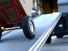 Homeowner moves boxes up a loading ramp to a moving truck using a dolly. Here are tips on how to pack to get your stuff moved safely and effectively.